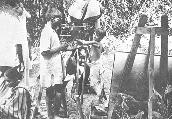 টুলের উপর দাঁড়িয়ে, অতি কষ্টে ক্যামেরায় চোখ লাগাতে চেষ্টা করছে অপু।